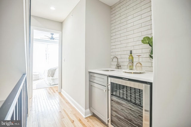 bar featuring light wood-type flooring, backsplash, ceiling fan, sink, and wine cooler