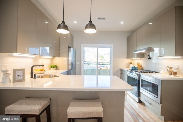 kitchen with a breakfast bar, hanging light fixtures, sink, appliances with stainless steel finishes, and kitchen peninsula