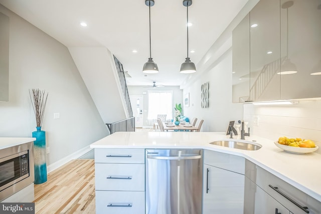 kitchen featuring ceiling fan, sink, hanging light fixtures, light hardwood / wood-style flooring, and appliances with stainless steel finishes