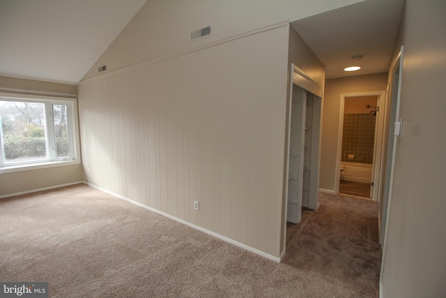 carpeted empty room with wooden walls and lofted ceiling