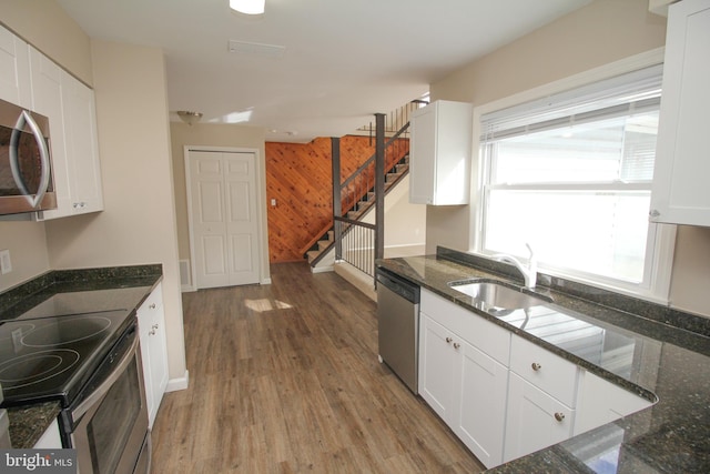 kitchen featuring stainless steel appliances, white cabinetry, wooden walls, and sink