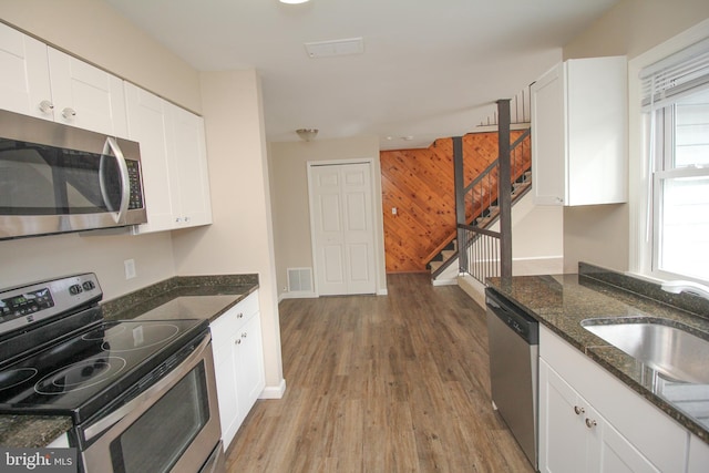 kitchen with wood walls, dark stone counters, sink, white cabinetry, and stainless steel appliances