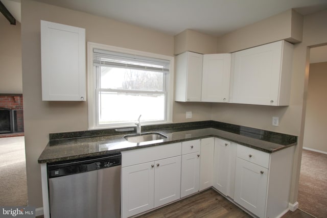 kitchen with dark carpet, stainless steel dishwasher, sink, a fireplace, and white cabinetry