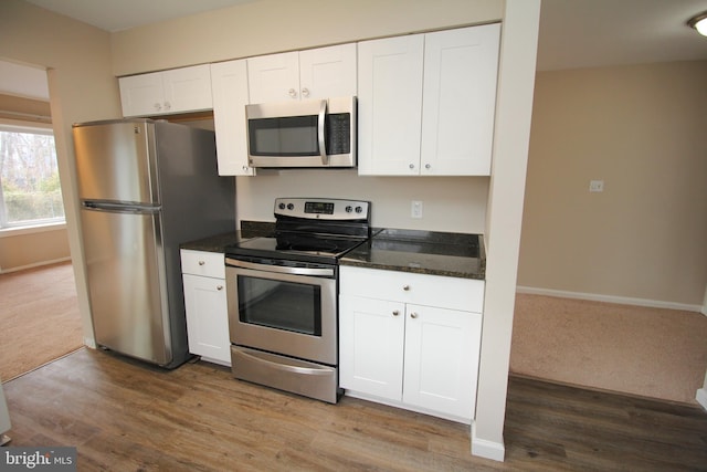 kitchen featuring dark stone countertops, white cabinetry, stainless steel appliances, and light hardwood / wood-style floors