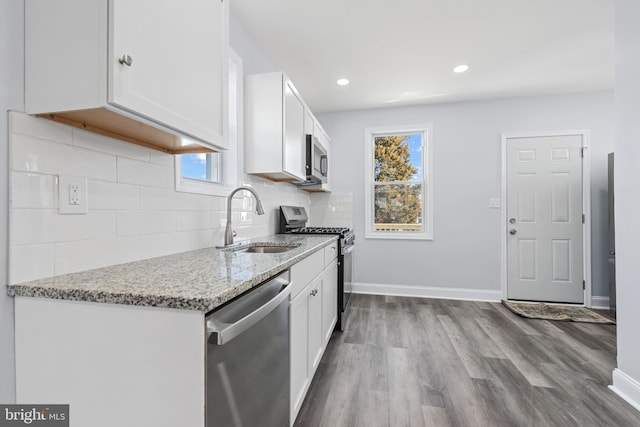 kitchen with tasteful backsplash, stainless steel appliances, light stone counters, sink, and white cabinetry