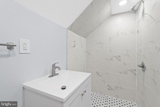 bathroom featuring vanity, vaulted ceiling, and tiled shower