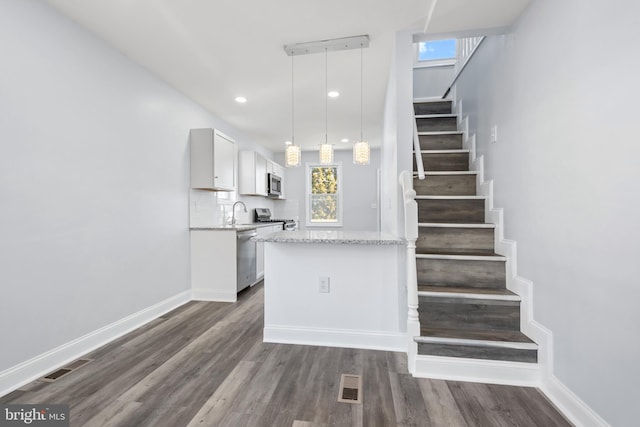 interior space with decorative light fixtures, tasteful backsplash, appliances with stainless steel finishes, white cabinets, and dark hardwood / wood-style floors