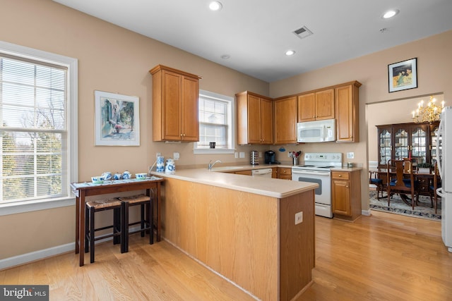 kitchen with white appliances, kitchen peninsula, sink, and light hardwood / wood-style flooring