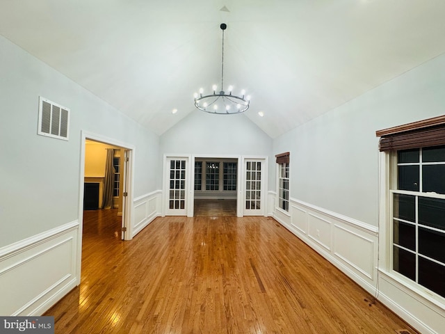 unfurnished living room featuring hardwood / wood-style flooring, a chandelier, and lofted ceiling