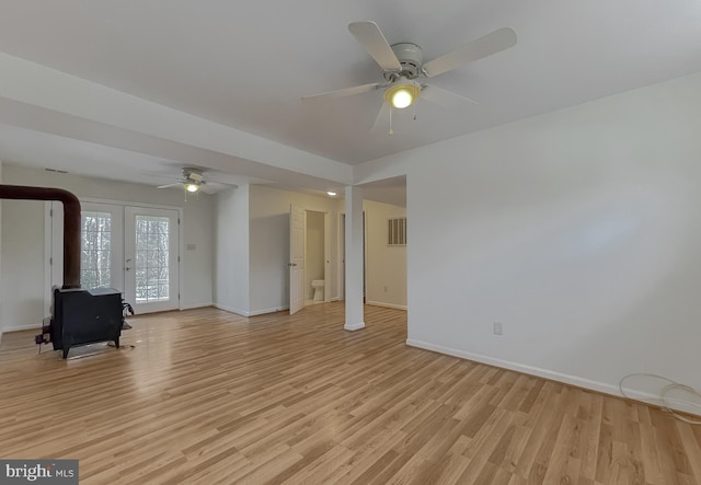 unfurnished living room with ceiling fan, french doors, a wood stove, and light hardwood / wood-style floors