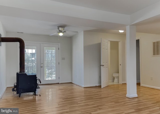 interior space with ceiling fan, french doors, a wood stove, and light hardwood / wood-style flooring