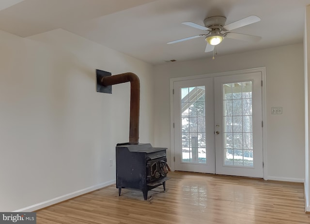 doorway to outside featuring light wood-type flooring, french doors, a wood stove, and ceiling fan