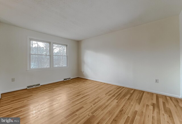 spare room with light hardwood / wood-style floors and a textured ceiling