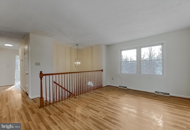 empty room featuring a notable chandelier, a textured ceiling, and light hardwood / wood-style flooring