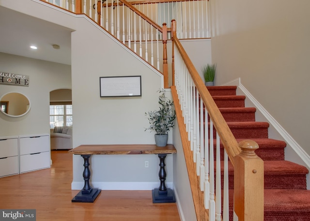 stairway with recessed lighting, wood finished floors, arched walkways, and baseboards