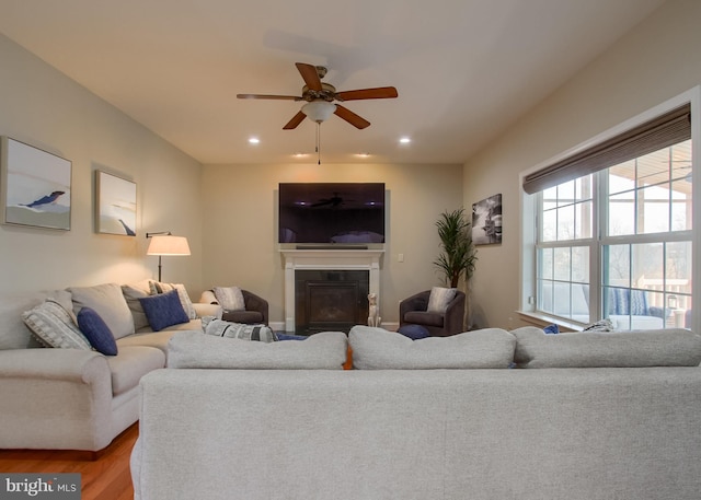 living area featuring a glass covered fireplace, a ceiling fan, wood finished floors, and recessed lighting