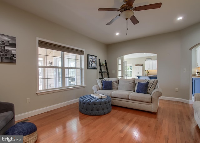 living area featuring recessed lighting, light wood-style floors, arched walkways, and baseboards