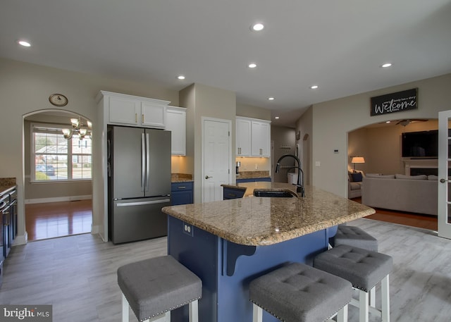 kitchen with a large island with sink, freestanding refrigerator, arched walkways, white cabinets, and a sink