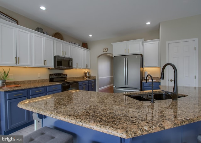 kitchen featuring blue cabinets, a breakfast bar, black electric range oven, freestanding refrigerator, and arched walkways