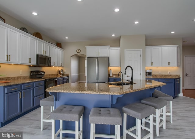 kitchen featuring blue cabinetry, freestanding refrigerator, black electric range, arched walkways, and a sink