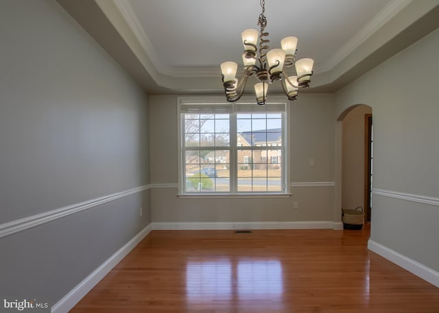 spare room with wood finished floors, baseboards, a tray ceiling, arched walkways, and ornamental molding