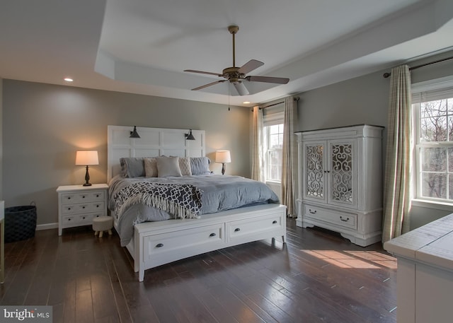 bedroom with a raised ceiling, a ceiling fan, dark wood-style floors, recessed lighting, and baseboards