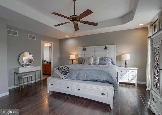 bedroom with a tray ceiling, visible vents, and dark wood finished floors