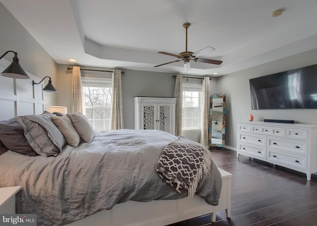 bedroom with a raised ceiling, multiple windows, and dark wood-style floors