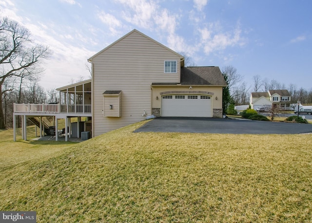 view of side of home featuring a deck, driveway, stone siding, a yard, and a sunroom