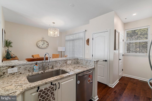 kitchen with light stone counters, sink, stainless steel dishwasher, and hanging light fixtures