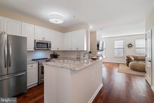 kitchen with appliances with stainless steel finishes, white cabinets, light stone counters, and kitchen peninsula