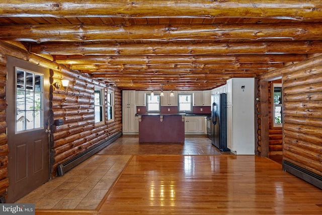 kitchen featuring black fridge, a baseboard heating unit, white cabinets, and log walls