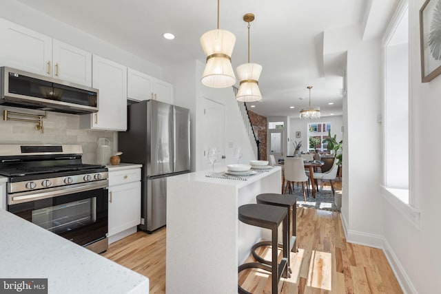 kitchen with white cabinets, appliances with stainless steel finishes, backsplash, and pendant lighting