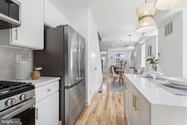 kitchen featuring light stone countertops, backsplash, stainless steel appliances, white cabinetry, and hanging light fixtures