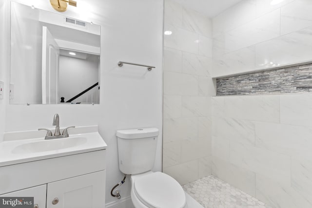 bathroom featuring a tile shower, vanity, and toilet