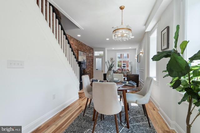 dining space with a notable chandelier, brick wall, and light hardwood / wood-style flooring