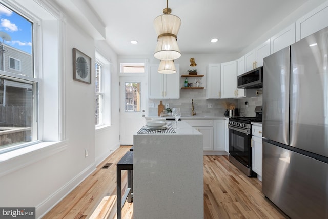 kitchen with pendant lighting, white cabinets, light wood-type flooring, tasteful backsplash, and stainless steel appliances