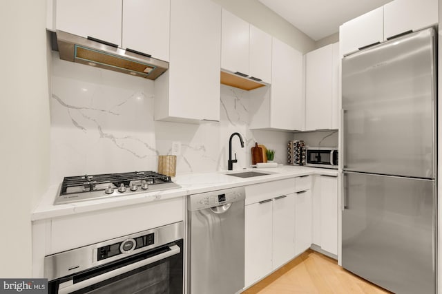 kitchen featuring appliances with stainless steel finishes, sink, white cabinets, light stone counters, and decorative backsplash