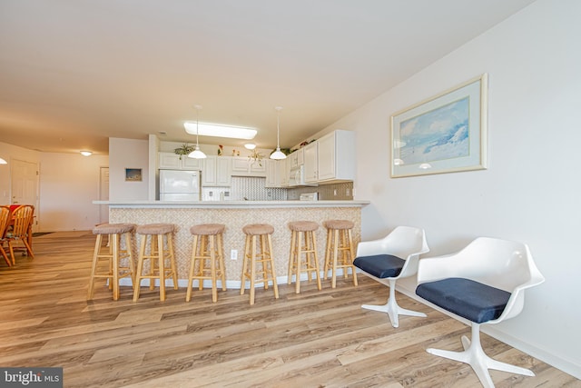 kitchen featuring white cabinets, decorative light fixtures, white fridge, backsplash, and a breakfast bar