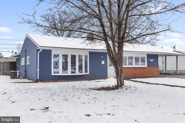 snow covered property with central AC, brick siding, and a chimney