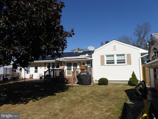 rear view of property featuring a wooden deck, a yard, and solar panels