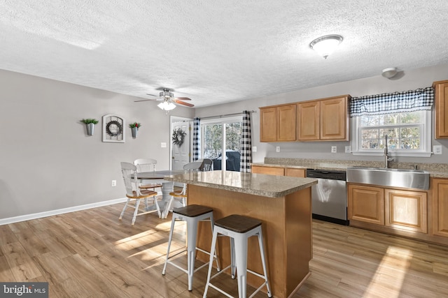 kitchen with a breakfast bar, sink, light wood-type flooring, stainless steel dishwasher, and a kitchen island