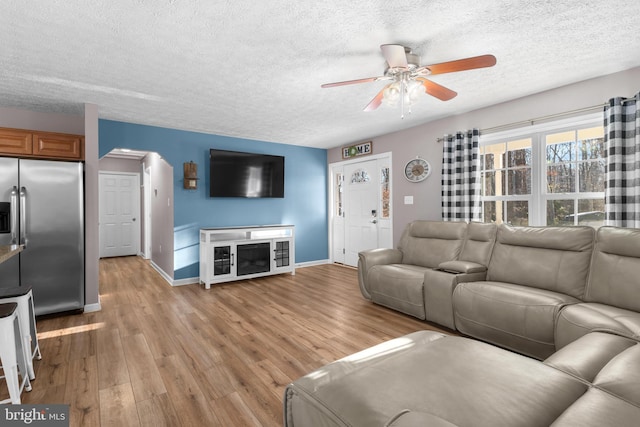 living room featuring ceiling fan, a textured ceiling, and light wood-type flooring