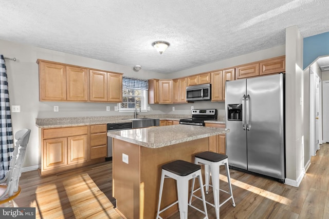 kitchen with sink, a kitchen breakfast bar, a center island, stainless steel appliances, and light wood-type flooring