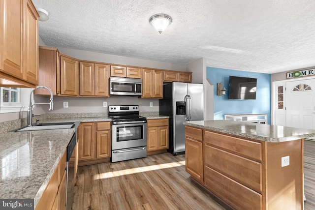 kitchen featuring a kitchen island, sink, hardwood / wood-style flooring, light stone counters, and stainless steel appliances