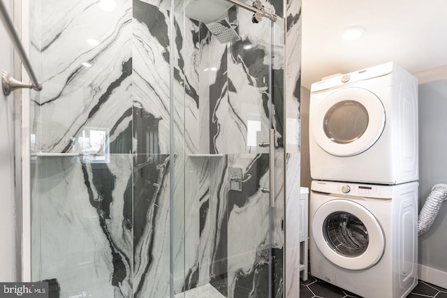 laundry room with dark tile patterned flooring and stacked washer and dryer