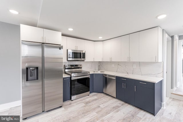 kitchen featuring light stone countertops, stainless steel appliances, blue cabinets, sink, and white cabinetry