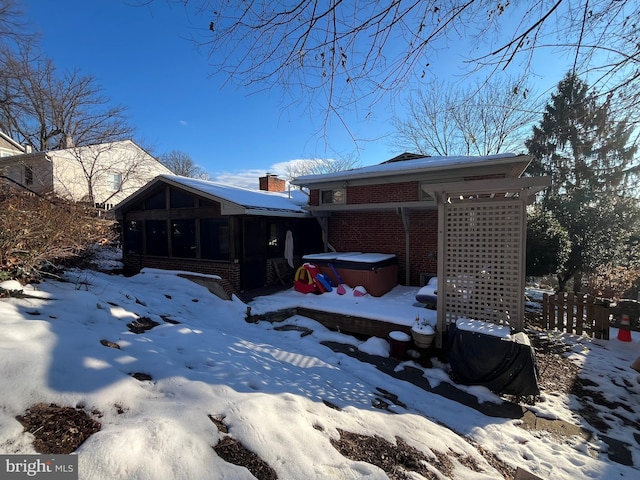 snow covered rear of property with a hot tub and a sunroom