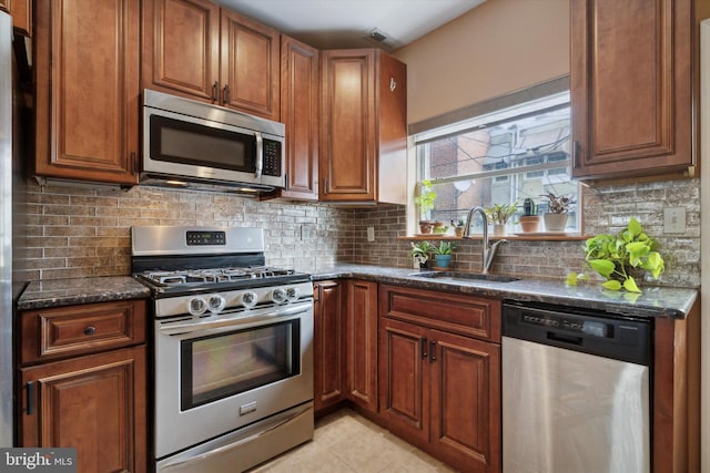 kitchen featuring light tile patterned flooring, sink, dark stone countertops, appliances with stainless steel finishes, and decorative backsplash