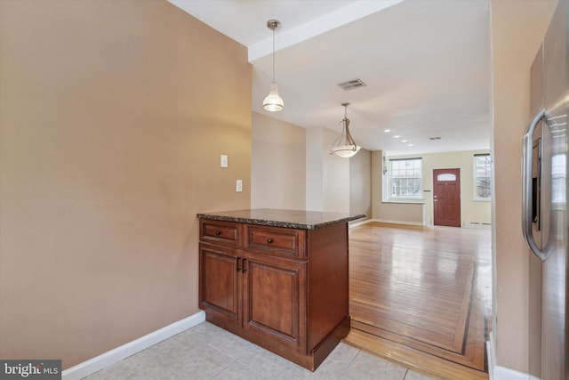 kitchen with stainless steel refrigerator, decorative light fixtures, dark stone counters, light tile patterned floors, and kitchen peninsula